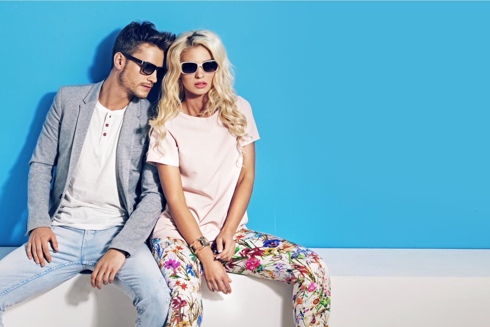 couple wearing sunglasses in front of blue wall