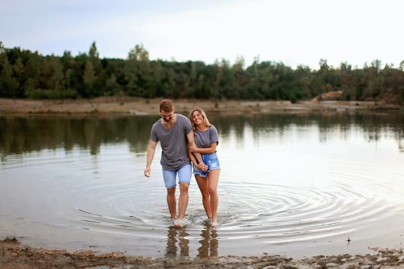 coppia che cammina sull'acqua bassa indossando top e pantaloncini grigi