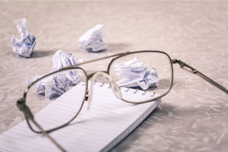 crumpled papers around a notebook and an eyeglasses