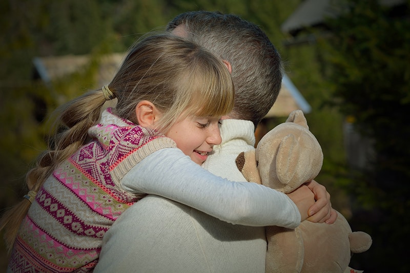 figlia che abbraccia il padre tenendo in mano l'orsacchiotto di peluche