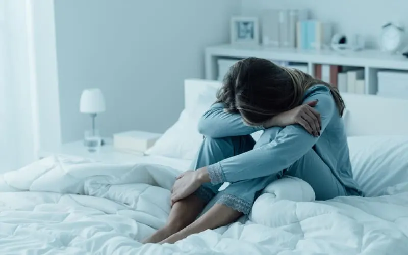 Depressed woman sitting in her bed with her head on her knees