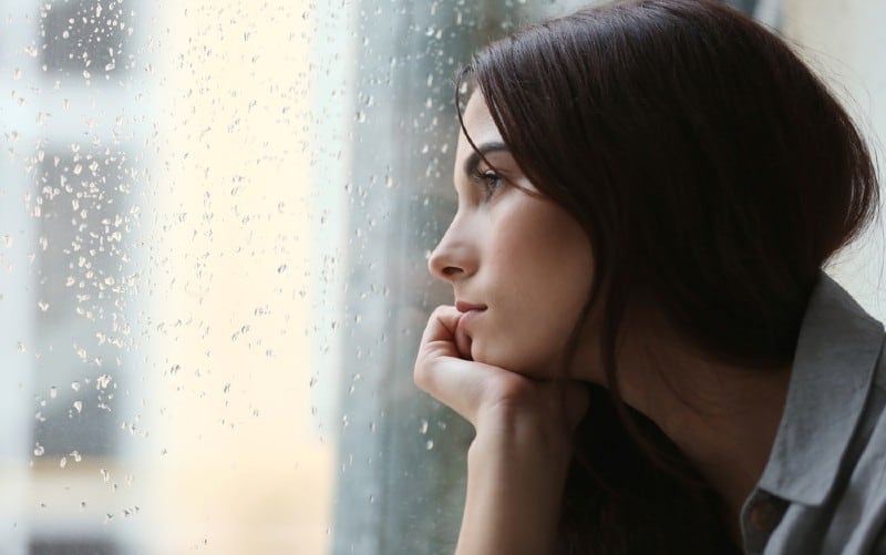 depressed young woman sitting near window