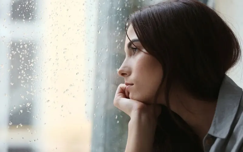 depressed young woman sitting near window