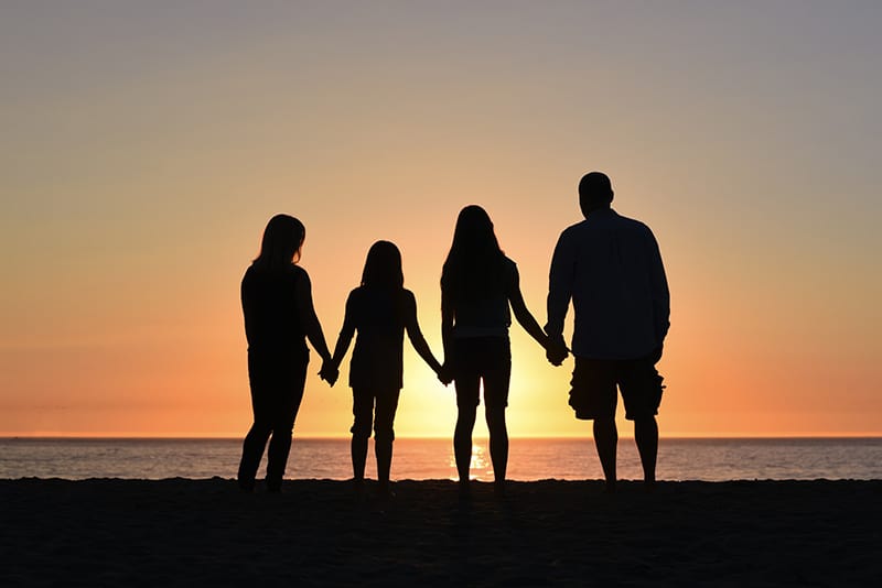 famiglia in piedi in riva al mare a guardare il tramonto