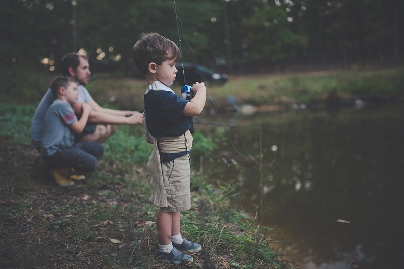 padre con due figli che pescano in riva al fiume