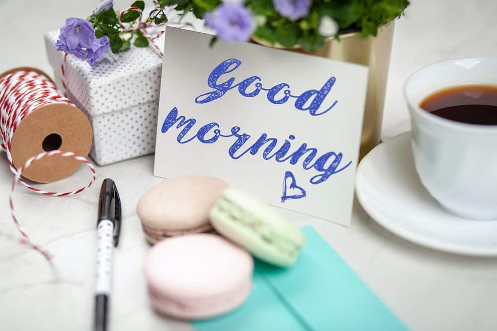 filled teacup with saucer beside good morning card and pen with macaroons