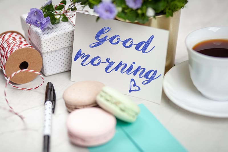 filled teacup with saucer beside good morning card and macaroons