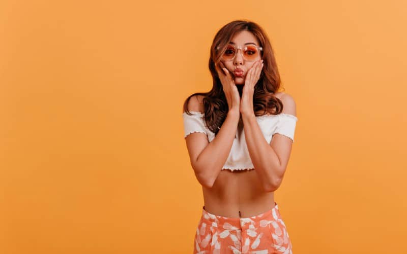 Funny woman with glasses making faces with pouted lips against orange wall