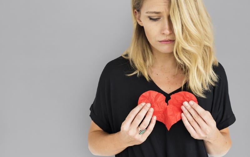 Ragazza con top nero che stringe al petto un cuore di carta spezzato