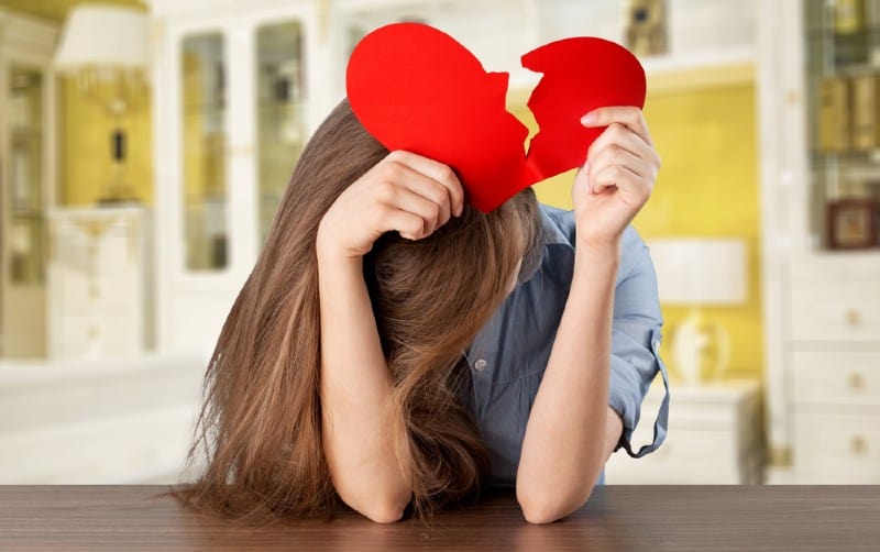 Sad lonely girl holding paper broken heart