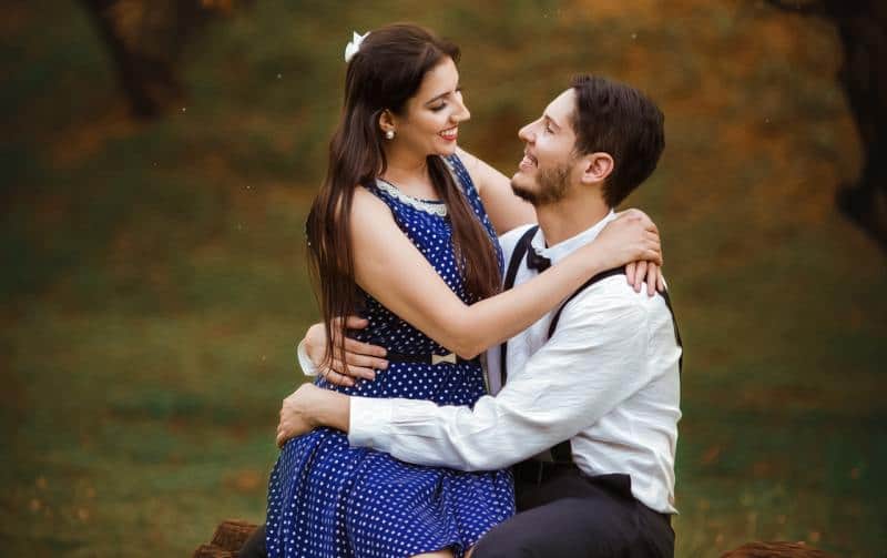 Beautiful girl wearing blue dress sitting on man's lap in the forest during daytime