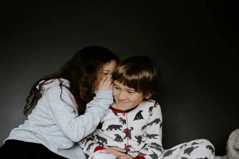girl whispering into boy's ear while sitting indoor