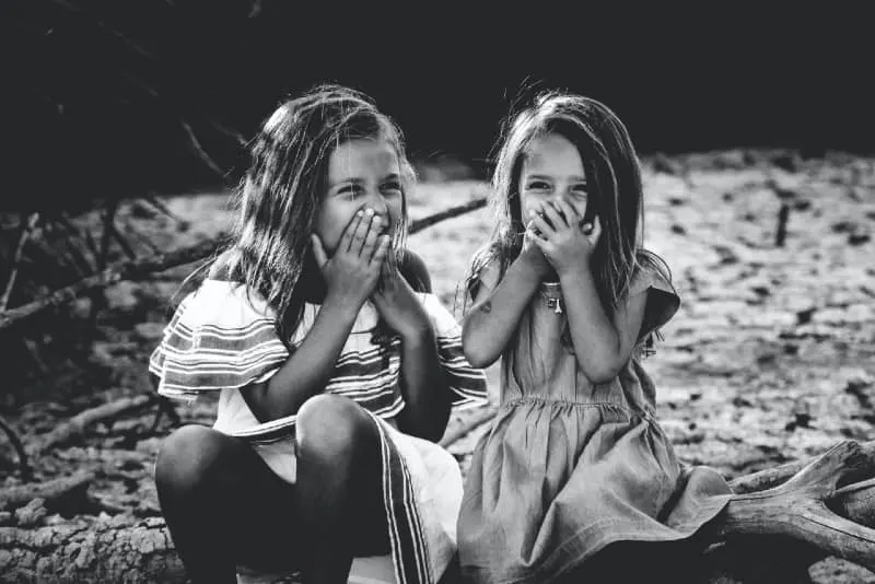 two girls closing their mouth and laughing