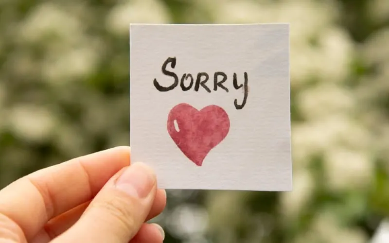 Hand holding sticker with sorry inscription and red heart