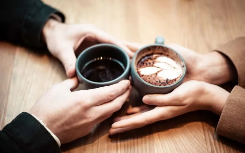 Hands of woman and man holding ceramic mugs with coffee