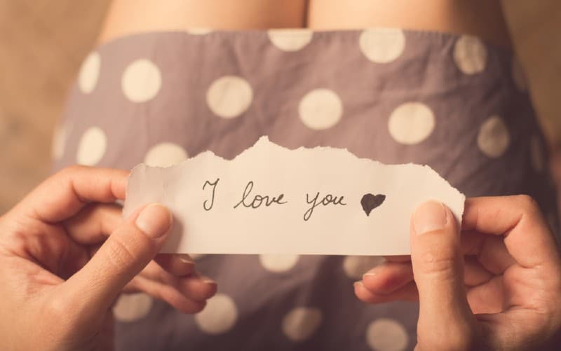 hands of a woman in dotten dress holding a paper with i love you message on it