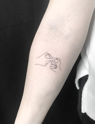mani che si tatuano il simbolo dell'infinito sul braccio