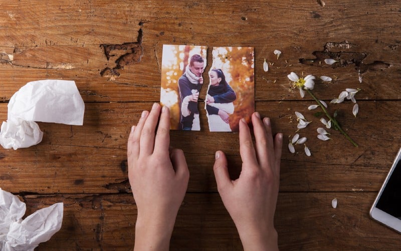 mani di una donna che toccano la foto strappata di una coppia su un tavolo di legno marrone