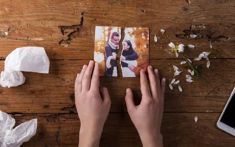 hands of a woman touching torn picture of a couple on a brown wooden table