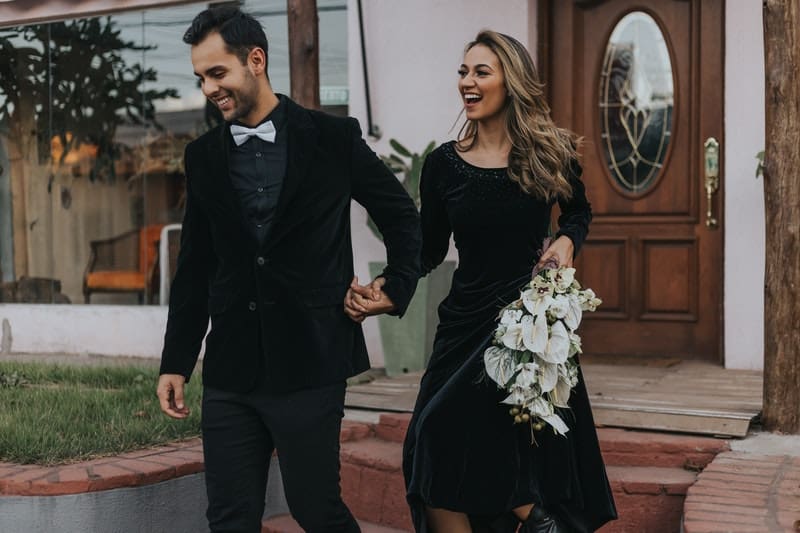 happy couple holding hands in black suit with flowers carried by the woman