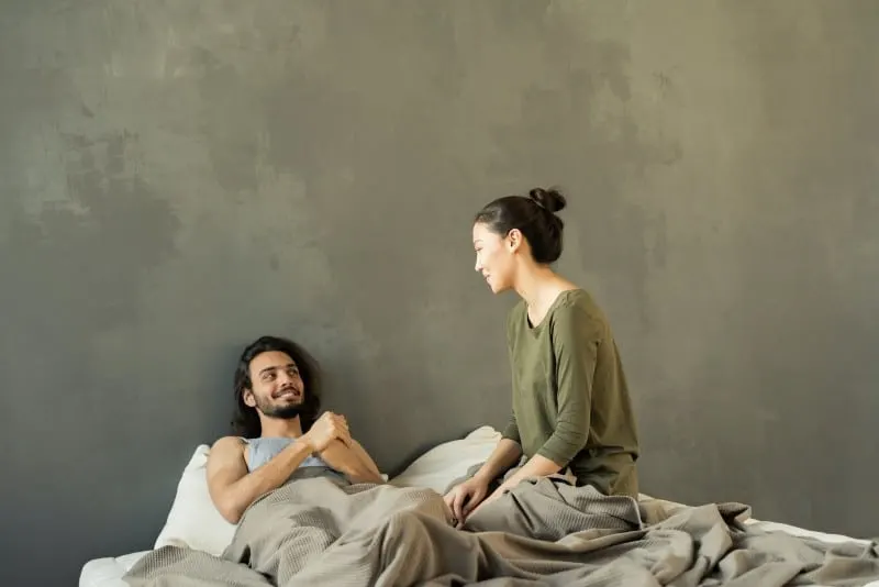 smiling man looking at woman in bed