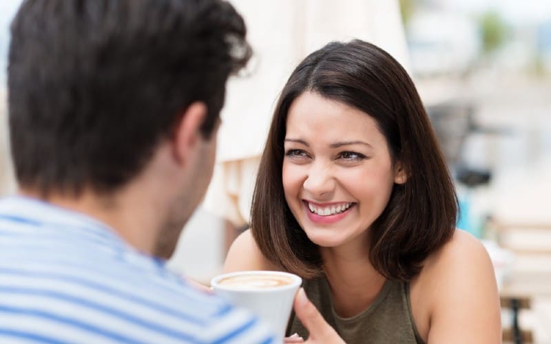 Donna felice seduta di fronte a un uomo con tazza di caffè durante il giorno