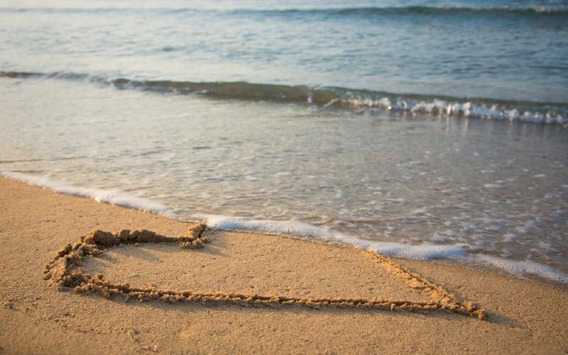 Cuore disegnato sulla sabbia della spiaggia che viene spazzato via da un'onda