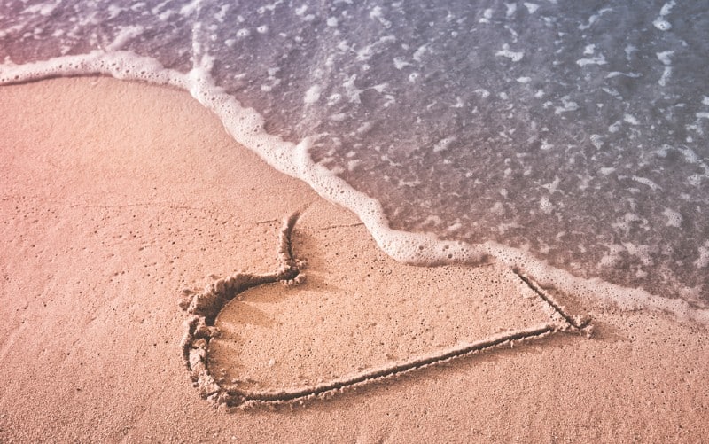 Cuore disegnato sulla sabbia della spiaggia che viene spazzato via da un'onda