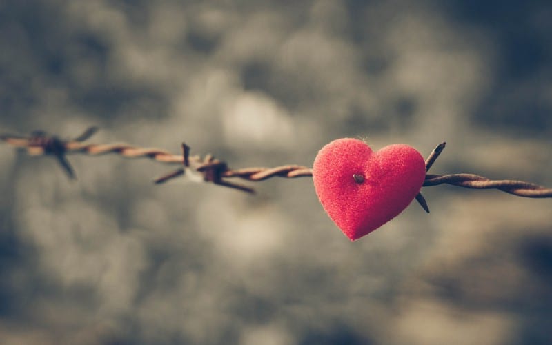 Corazón rojo sobre fondo de alambre de espino y cielo nublado