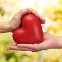 Mano de hombre y mujer sosteniendo corazón rojo