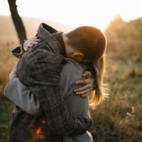 man and woman hugging each other on the field with sunlight