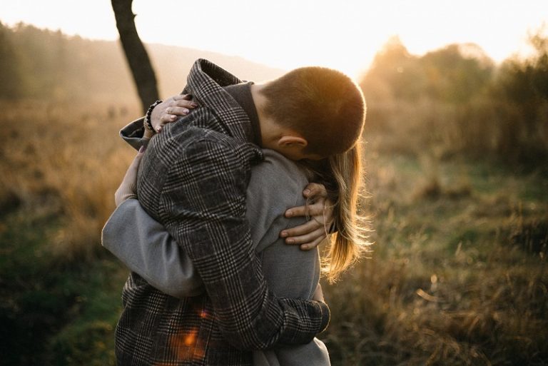 man and woman hugging each other on the field with sunlight