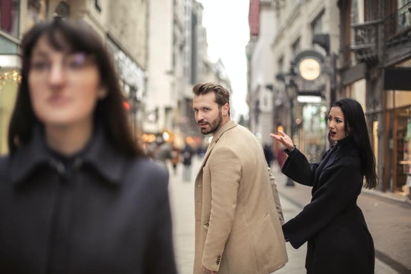 donna gelosa in impermeabile mentre il suo uomo guarda l'altra donna