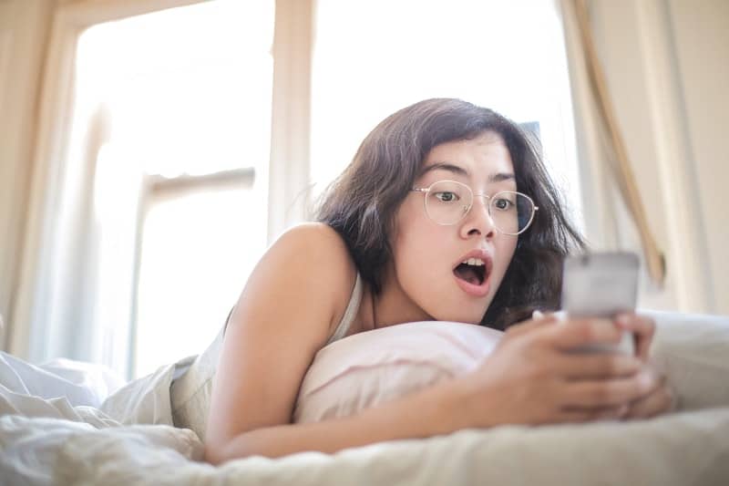 señora tumbada en la cama con gafas en la celebración de un teléfono móvil