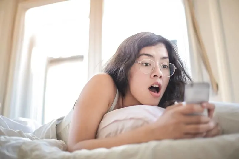 lady lying on bed with eyeglass on holding a cellphone