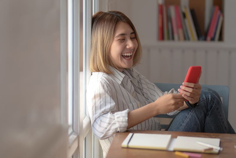 laughing woman using a smartphone while leaning on the wall