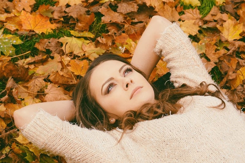 mujer tumbada sobre hojas con las manos en la cabeza