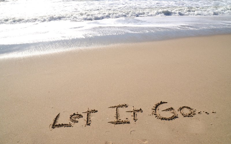 Let it go written on beach sand near the sea