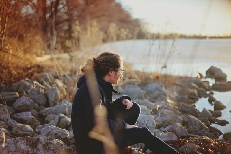 mujer solitaria en otoño sentada cerca del lago