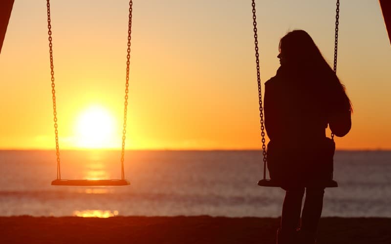 Lonely woman swinging on the beach at sunset time