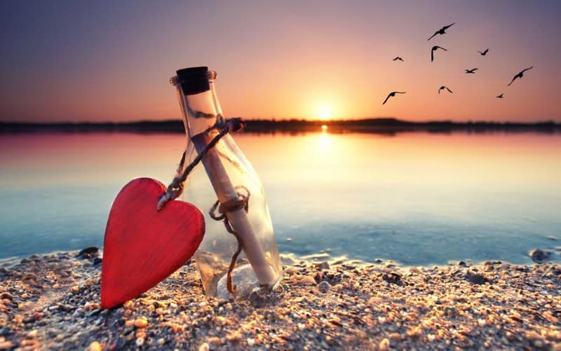 Messaggio d'amore in bottiglia con cuore rosso sulla spiaggia
