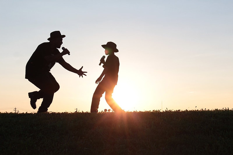 homem e rapaz a dançar e a cantar durante o pôr do sol