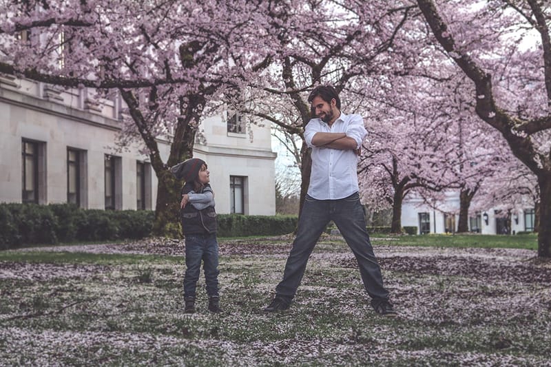 man and boy standing on the grass surrounded with trees