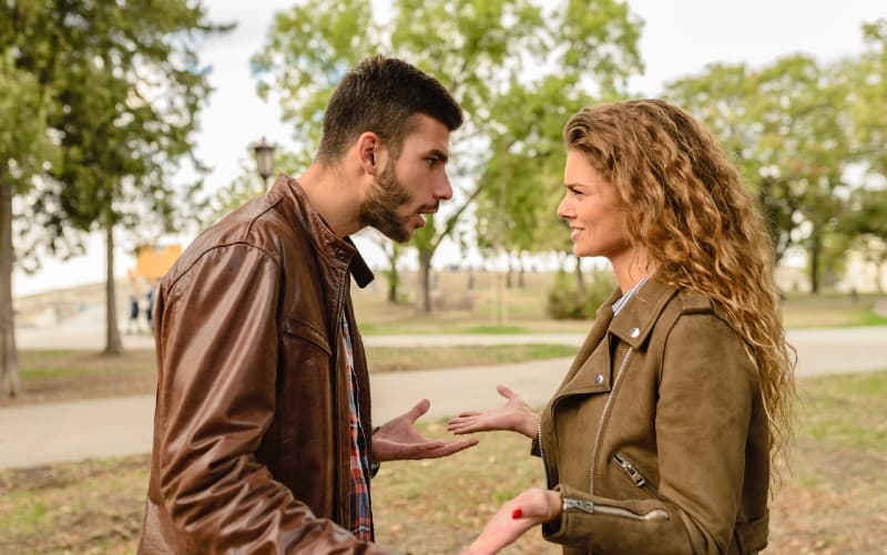 Hombre y mujer con chaqueta de cuero marrón discutiendo en un parque durante el día