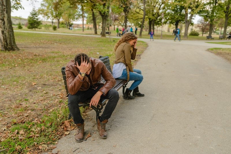 uomo e donna alla panchina che si tengono entrambi la testa