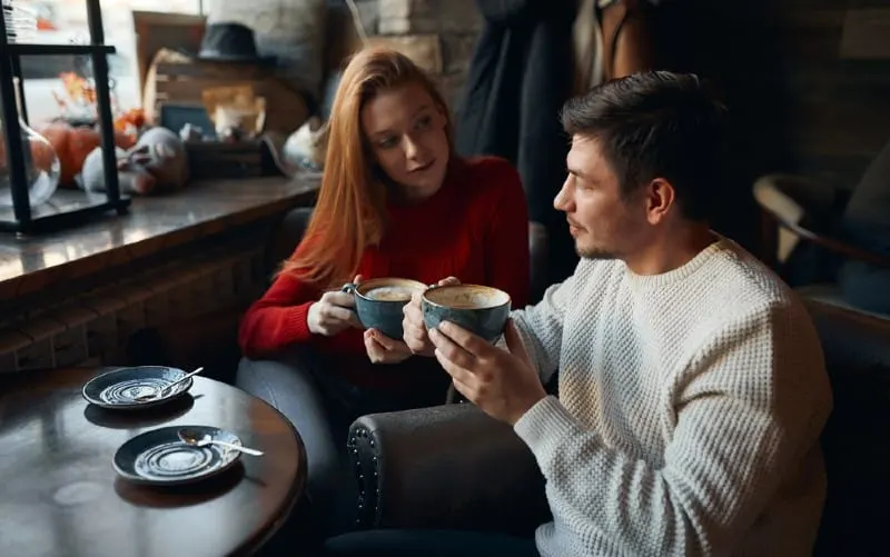 Man and woman drinking coffee sitting next to each other at a table