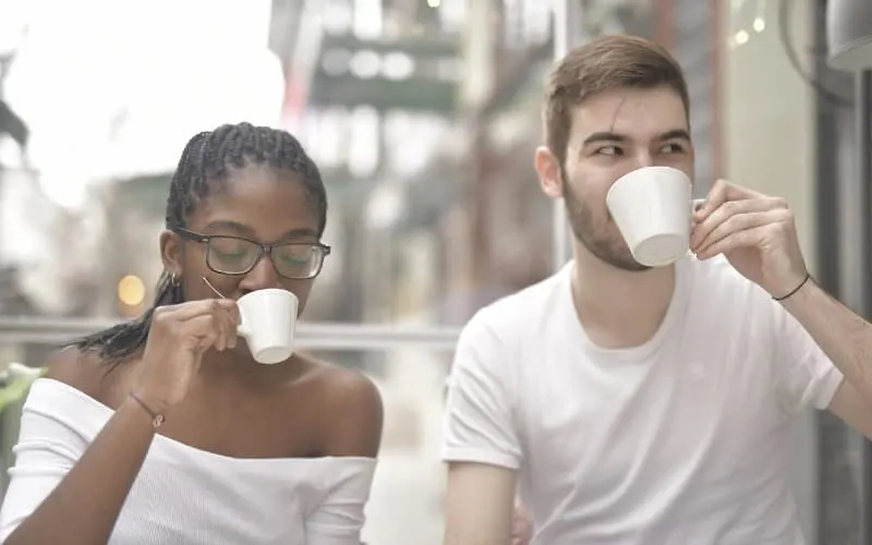 man and woman drinking from white ceramic mugs outdoors during daytime