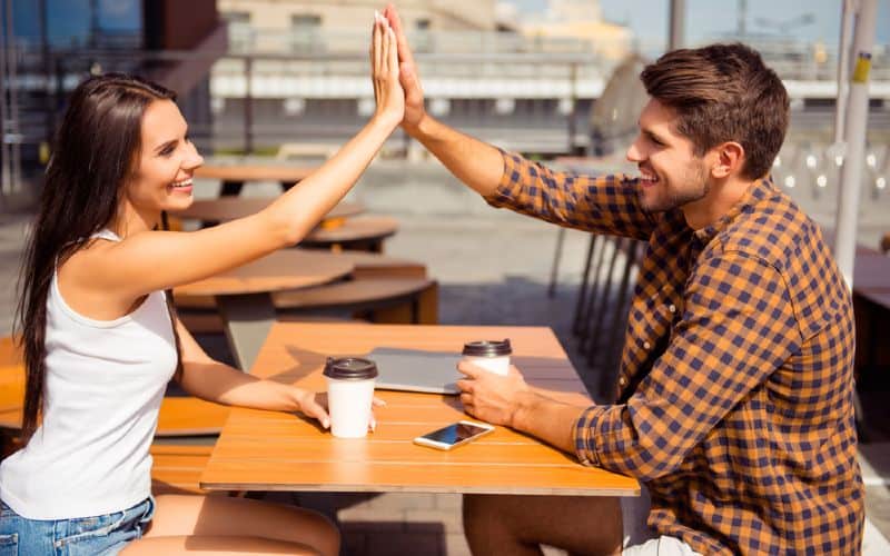 Happy man and woman sitting at a table in front of each other giving high five
