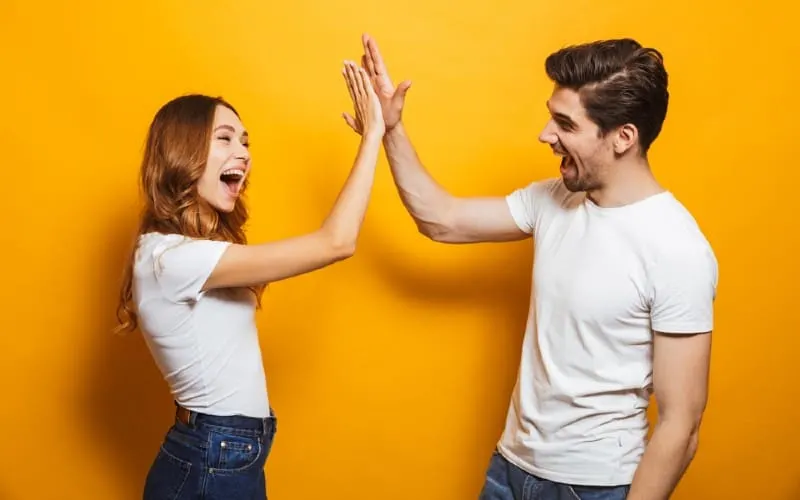 Man and woman giving high five standing near yellow wall