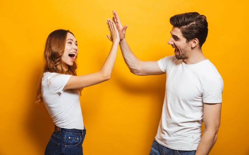 Hombre y mujer felices chocando los cinco contra una pared naranja